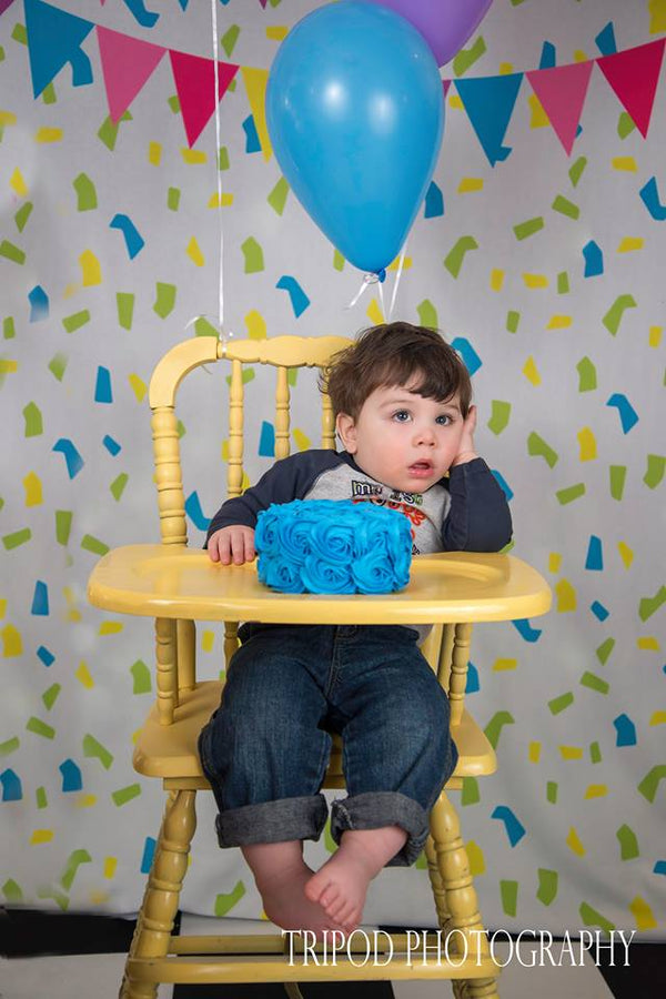 boy eating cake at highchair in front of birthday backdrop