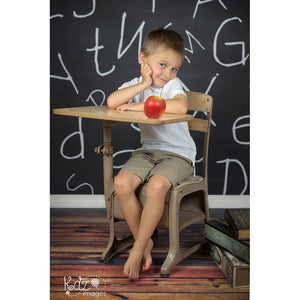 Boy sitting at school desk in front of chalkboard letter backdrop